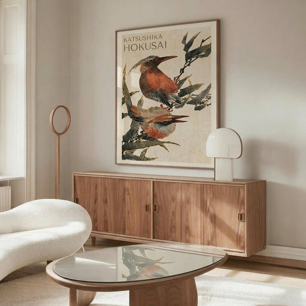 May include: Japanese-style bird print displayed above wooden sideboard in modern living room. Two colorful birds with reddish-brown and blue plumage perch on leafy branches against cream background. Framed artwork positioned over mid-century walnut credenza with sliding doors. White sculptural chair and glass coffee table with wood base visible. Minimalist spherical table lamp and floor lamp complete the scene.