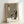 May include: Framed poster print leaning against white wall showing minimalist illustration of black cat character with large white eyes sitting beside white paper lantern with cherry blossom design and Japanese characters above on textured beige background, displayed in light wooden frame
