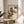 May include: Framed vintage Japanese bird artwork displayed on round wooden side table next to beige upholstered chair. Print features two colorful birds with orange-red breasts and long curved beaks perched among green foliage against cream background. Natural lighting creates soft shadows across neutral-toned room with plant visible in corner.