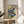 May include: Japanese woodblock print artwork in wooden frame showing a dramatic waterfall cascading over orange-red cliffs with blue and white water, surrounded by green foliage. The framed print sits on a light wood round side table next to a beige upholstered chair, with a potted plant visible in soft natural lighting from nearby windows.
