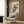 May include: Japanese woodblock print artwork featuring two orange and brown birds perched on green branches, displayed in white frame on wood-paneled wall above beige upholstered armchair with geometric patterned pillow, brass floor lamp and side table with open book nearby