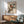 May include: Framed vintage Japanese woodblock print featuring two colorful birds perched on flowering branches, displayed above a mid-century modern wooden credenza with lamp in bright living room setting with sage green upholstered chair