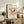 May include: Abstract art poster with intricate black line drawings featuring organic and geometric shapes, displayed in light wood frame on rustic wooden sideboard. Room scene shows beige upholstered chair, fern plant, ceramic vase, stacked books, and warm neutral lighting against cream walls.
