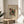 May include: Abstract art print by Wassily Kandinsky featuring colorful geometric shapes in red, yellow, black, and teal with scattered dots and lines, displayed in light wood frame on round wooden side table next to beige upholstered chair with plant leaves visible in soft natural lighting