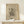 May include: Framed abstract art print in light wood frame displaying geometric black line drawings and shapes on beige background, leaning against white wall on light wooden surface beside small white gift box with twine and greenery accent.