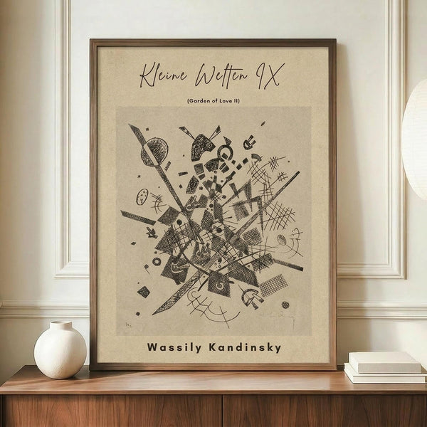 May include: Framed abstract art print in warm brown wooden frame displaying geometric black line drawings and shapes on beige background, positioned on wooden sideboard next to white ceramic vase and stacked books against cream wainscoted wall in modern interior setting.