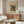 May include: Abstract modernist art print with colorful geometric shapes, patterns, and forms in red, yellow, green, and black displayed in thin wooden frame above walnut credenza. Modern living room scene with white curved chair, glass oval coffee table, and minimalist white table lamp. Warm natural lighting on light colored walls.