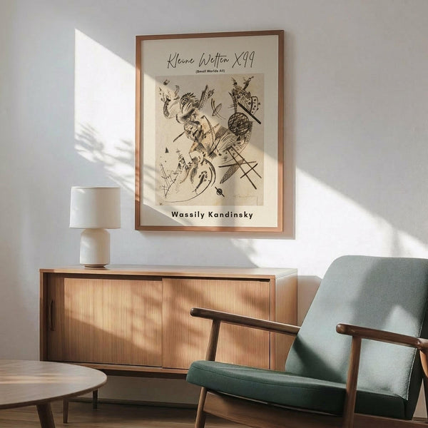 May include: Framed abstract art print with black line drawings on cream background, featuring geometric shapes and organic forms in Kandinsky's style. Wooden frame hangs above mid-century modern walnut credenza with white ceramic lamp. Sage green upholstered armchair with wooden arms sits nearby. Warm sunlight creates diagonal shadows across white wall in minimalist living room setting.