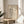 May include: Framed abstract art print with geometric black line drawings on cream background, displayed on round wooden side table next to beige upholstered chair. Natural lighting creates soft shadows across neutral-toned room with plant visible in corner. Artwork features angular shapes, dots, and flowing lines in minimalist style within thin wooden frame.