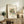 May include: Framed abstract art print with colorful geometric shapes in yellow, teal, and gray displayed on rustic wooden sideboard next to fern plant, books, and ceramic vase in warm, neutral-toned living room setting with beige upholstered furniture