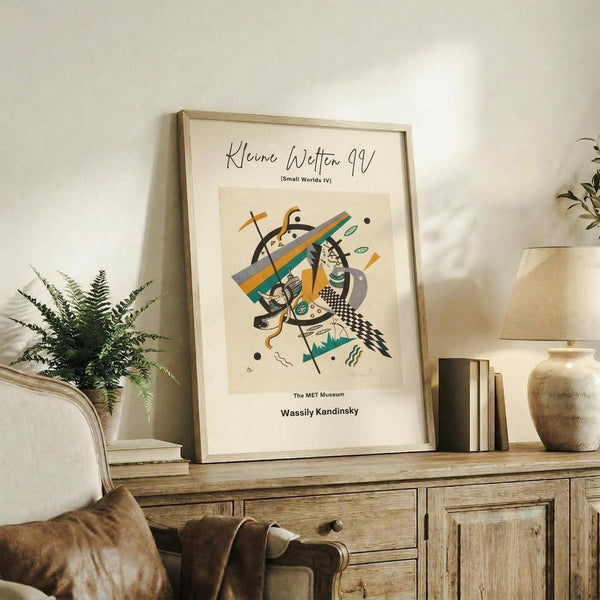 May include: Framed abstract art print with colorful geometric shapes in yellow, teal, and gray displayed on rustic wooden sideboard next to fern plant, books, and ceramic vase in warm, neutral-toned living room setting with beige upholstered furniture
