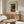 May include: Vintage Japanese woodblock print poster featuring a moonlit lake scene with traditional buildings, trees, and mountains in blue and earth tones, displayed in beige matting above a mid-century modern walnut credenza. Room shows minimalist decor with white curved chair, glass oval coffee table, and modern table lamps in neutral tones.