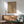 May include: Framed abstract art print with geometric line drawings on beige background, displayed above wooden sideboard with table lamp. Modern mint green upholstered chair with wooden arms sits beside round coffee table. Warm sunlight creates shadows across white wall in minimalist living room setting.