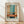 May include: Framed abstract art print leaning against white wall on light wooden floor. Poster features horizontal blocks of teal blue, cream, orange and coral colors in painterly style with soft edges and texture. French text at top, artist name and quote at bottom. Natural wood frame with white matting. Soft window light creates diagonal shadows across white textured wall.