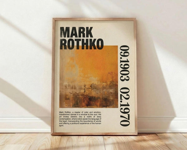 May include: Framed poster with Mark Rothko's name in bold black letters, featuring an abstract painting with warm orange and brown tones that fade from bright yellow-orange at top to darker earthy browns below. The years 1903-1970 appear vertically along the right side. Descriptive text about the artist sits below the artwork. The cream-colored poster is displayed in a thin wooden frame, leaning against a white wall on light wooden flooring with soft natural lighting.