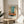 May include: Framed abstract art print with turquoise, orange, and cream color blocks in Rothko's signature style, displayed on round wooden side table next to beige upholstered chair. Natural sunlight creates geometric shadows on white wall. Green plant leaves visible in corner. Print features French text at top and artist name at bottom in clean typography.