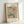 May include: Framed botanical art print featuring William Morris's ornate floral pattern in muted greens, blues, coral pink, and cream colors. The vintage-style design shows intertwining leaves, flowers, and decorative elements. Text above and below identifies it as "Lodden Famous Pattern" from 1884 by the Smithsonian Institution. Natural wood frame sits against white wall with soft lighting creating gentle shadows.