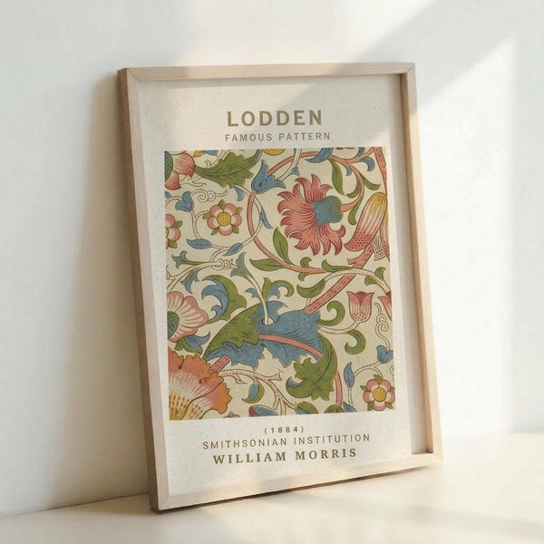 May include: Framed botanical art print featuring William Morris's ornate floral pattern in muted greens, blues, coral pink, and cream colors. The vintage-style design shows intertwining leaves, flowers, and decorative elements. Text above and below identifies it as "Lodden Famous Pattern" from 1884 by the Smithsonian Institution. Natural wood frame sits against white wall with soft lighting creating gentle shadows.