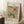 May include: Framed botanical art print with ornate floral pattern in coral, blue, and green tones featuring swirling leaves and decorative flowers. Light wood frame leans against white paneled wall next to wooden side table with white coffee cup. Cream textured rug and beige throw blanket visible in cozy room setting with natural window light casting soft shadows.