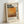 May include: Framed poster print leaning against white wall featuring Mark Rothko's name in bold black letters, orange and brown abstract painted artwork, biographical text, and birth/death years displayed vertically. Light wood frame surrounds cream-colored background with warm lighting creating soft shadows.