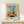 May include: Framed abstract art print displayed on light wood surface against cream wall. Artwork features vertical bands of turquoise blue, coral orange, cream, and dark navy in Rothko's signature color field style. Thin natural wood frame with white matting. Small white wrapped gift box with twine and greenery sprig sits in front. French text visible at top of print.