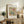 May include: Framed botanical print featuring William Morris's colorful floral pattern with pink flowers, green leaves, and blue accents on cream background. Print displays against white wall on rustic wooden sideboard alongside fern plant, ceramic vase, stacked books, and neutral upholstered furniture in warm, natural lighting.