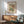 May include: Framed poster featuring William Morris floral pattern with colorful botanical design in green, coral, and blue tones, displayed above mid-century modern wooden credenza with white ceramic table lamp, next to sage green upholstered armchair with wooden frame in bright, naturally-lit room with white walls and warm wood furnishings.