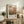 May include: Framed art print featuring Mark Rothko's name and abstract color blocks in warm earth tones - beige, brown, and orange rectangles. Print displays birth and death years 1903-1970 with descriptive text below. Shown in light wood frame on rustic wooden sideboard alongside fern plant, ceramic vases, books, and leather cushions in neutral-toned living room setting.