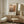 a living room with a large framed poster of an abstract painting hanging on the wall, a white armchair, a wooden sideboard, and a small round table.