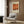 May include: Modern beige armchair with geometric patterned pillow in contemporary living room setting with wood paneled wall. Framed vintage-style art poster featuring orange and rust colored abstract painting with "Mark Rothko" text and dates "1903-1970" hangs above chair. Gold floor lamp with white marble base and open book on dark side table complete the styled interior scene.