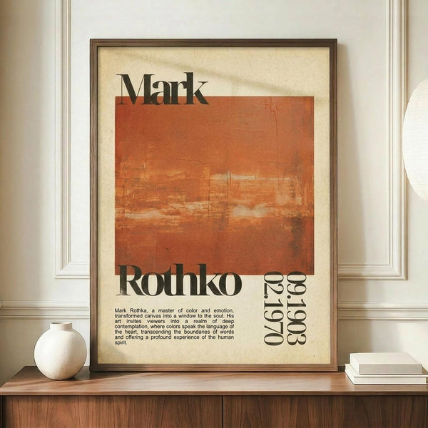 May include: Framed vintage-style poster featuring Mark Rothko's name and dates (1903-1970) with an abstract orange and rust-colored rectangular painting reproduction. The cream and orange poster is displayed in a dark wooden frame on a mid-century modern wooden credenza alongside a white ceramic vase and stack of books. Warm natural lighting creates soft shadows on the white paneled wall behind.