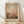 May include: Framed art print featuring an abstract landscape painting with soft gradient colors transitioning from muted green-gray at top to warm peach and coral tones, with darker brown landscape elements at bottom. The artwork has a dreamy, atmospheric quality with blended brushstrokes. Displayed in light wood frame with cream matting, leaning against white wall on light wooden floor with natural window light casting diagonal shadows.