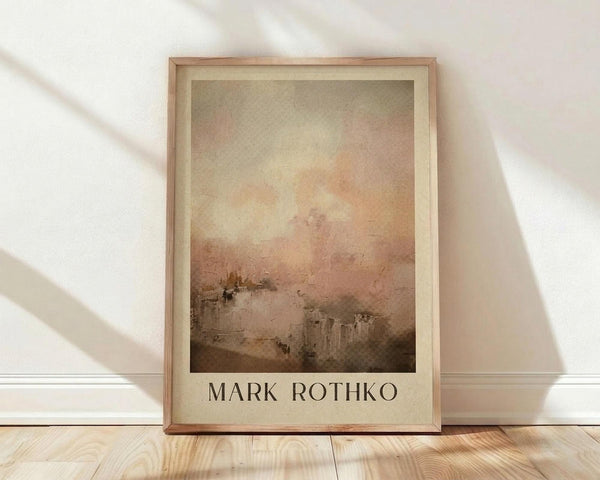 May include: Framed art print featuring an abstract landscape painting with soft gradient colors transitioning from muted green-gray at top to warm peach and coral tones, with darker brown landscape elements at bottom. The artwork has a dreamy, atmospheric quality with blended brushstrokes. Displayed in light wood frame with cream matting, leaning against white wall on light wooden floor with natural window light casting diagonal shadows.