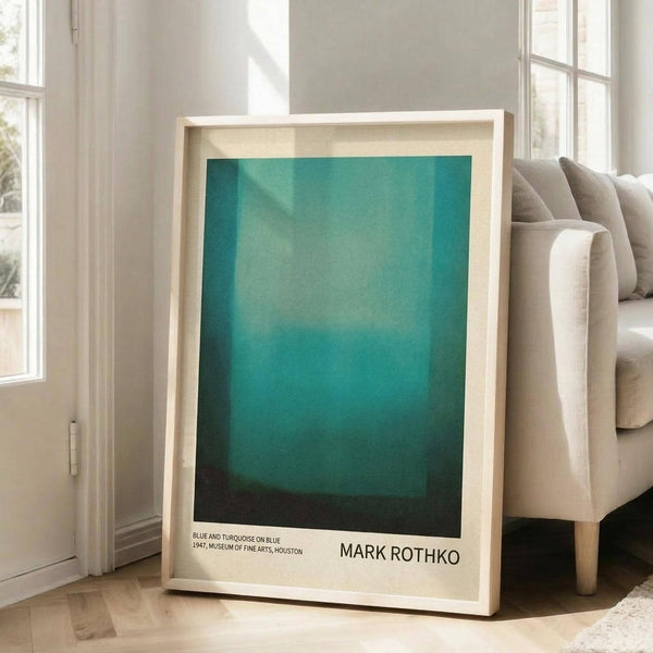 May include: A framed art print featuring Mark Rothko's abstract painting with gradient turquoise and teal color fields, displayed in a light wood frame against a beige couch in a bright living room with white walls and large windows. The poster shows smooth color transitions from lighter turquoise at top to deeper teal at bottom, with museum exhibition text below the artwork.
