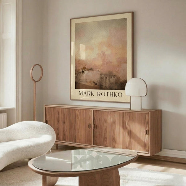 May include: Abstract art poster with warm orange, pink and brown tones in thin wooden frame, displayed above walnut credenza in minimalist living room with white curved chair, glass coffee table, and modern lamp on neutral walls
