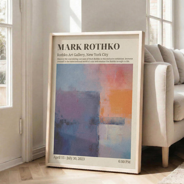 May include: Framed abstract art exhibition poster leaning against white wall next to beige sofa. Features colorful rectangular blocks in blues, oranges, purples and grays with black text describing gallery show dates. Natural light streams through windows onto light wooden floors in minimalist living room setting.