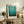 May include: Framed Mark Rothko museum poster featuring gradient blue and turquoise color blocks, displayed on rustic wooden sideboard in warm-toned living room with fern plant, ceramic vase, books, and cream upholstered chair with brown leather throw pillow