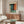 a modern living room with a large abstract painting hanging on the wall above a wooden cabinet. The room has a white sofa, a glass coffee table, and a lamp on a side table.