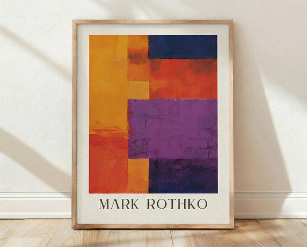May include: Framed abstract art print with bold rectangular color blocks in orange, yellow, red, navy blue, and purple, displayed in light wood frame with white matting against white textured wall on wooden floor with natural window light creating soft shadows