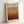 May include: Framed poster with warm gradient design transitioning from golden yellow at top to deep burgundy at bottom, creating layered horizontal bands reminiscent of abstract landscape. Text at top reads "MARK ROTHKO" with gallery information and exhibition dates "April 15 - July 30, 2023" and "6:00 PM" at bottom. Light wood frame against white wall with soft shadow.