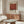 May include: Mark Rothko exhibition poster featuring large rust-red square on cream background with black text, displayed above wooden sideboard in minimalist room with white curved chair, glass coffee table, and neutral walls