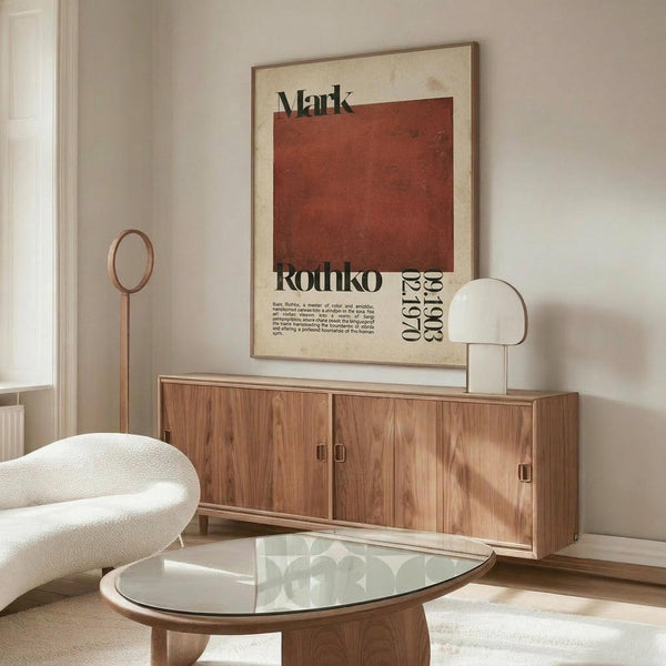 May include: Mark Rothko exhibition poster featuring large rust-red square on cream background with black text, displayed above wooden sideboard in minimalist room with white curved chair, glass coffee table, and neutral walls