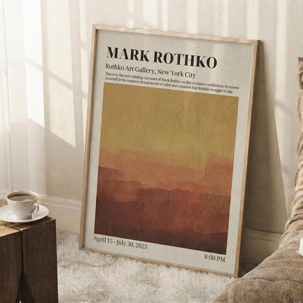 May include: Framed art poster leaning against white wall corner featuring abstract landscape in warm gradient tones from golden yellow to deep rust red. Light wood frame, displayed on white textured rug beside wooden side table with white coffee cup and saucer. Natural window light creates soft shadows on wall.