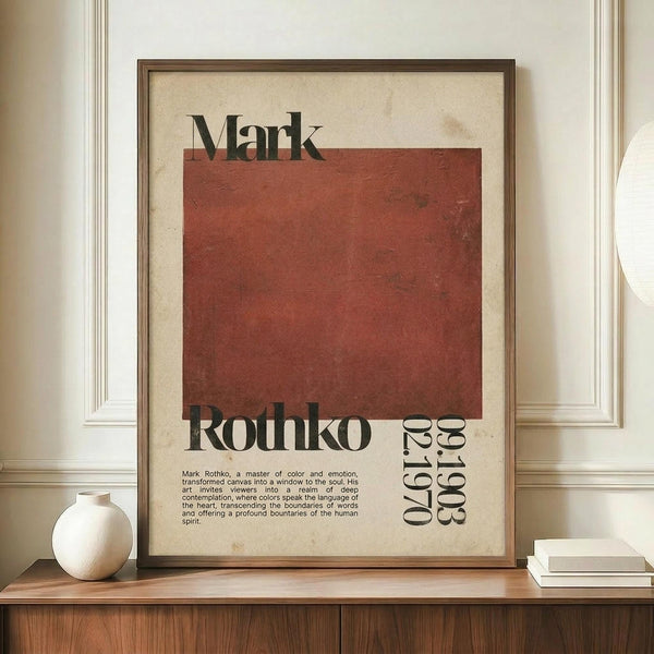 May include: Framed vintage-style poster with cream background and large rust-red square, featuring "Mark Rothko" in bold black text and biographical description below. Wooden frame sits on mid-century modern credenza beside white ceramic vase and stacked books against cream paneled wall.