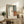 May include: Abstract art print with soft blue, white, orange and dark vertical forms in light wood frame, displayed on rustic wooden console table alongside fern plant, ceramic vase, stacked books and leather armchair in warm neutral living room setting