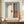 May include: Framed abstract art print in earth tones with vertical composition featuring cream, blue-gray, rust orange, and dark brown color blocks in soft, blended brushstrokes. The poster is displayed on a wooden sideboard alongside a white ceramic vase and stacked books in an elegant room with cream walls and decorative molding.