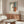 a modern living room with a large abstract painting hanging on the wall above a wooden cabinet. The room has a white sofa, a glass coffee table, and a lamp on a side table.