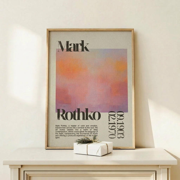 May include: Framed poster print featuring Mark Rothko's name above a gradient square in warm orange, pink and purple tones, with exhibition text below. Displayed on light wood surface with small wrapped gift beside it. Natural lighting creates soft shadows on cream wall background.