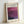 May include: Framed exhibition poster featuring Mark Rothko's abstract purple and magenta color field painting. Light wood frame displays white poster with black text reading "MARK ROTHKO" and "Rothko Art Gallery, New York City" above vibrant layered purple artwork. Exhibition dates April 15 - July 30, 2023 shown at bottom. Frame leans against white wall casting subtle shadow.