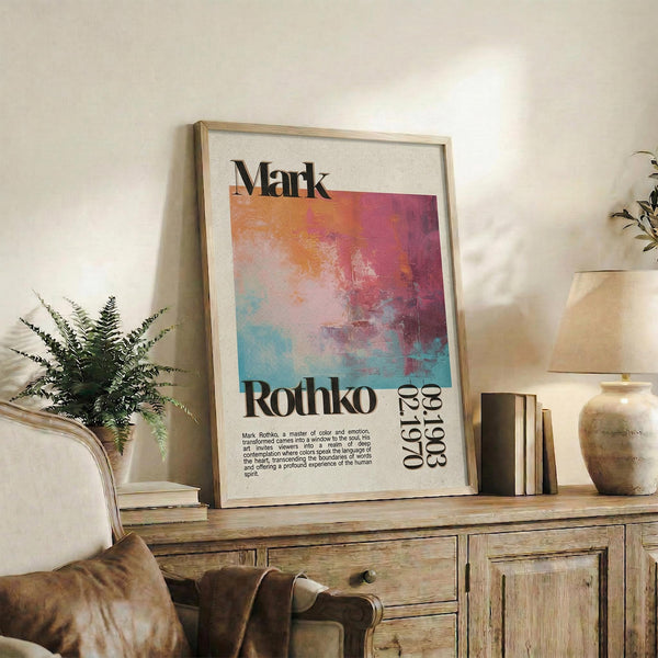 May include: Framed art poster with Mark Rothko's name and abstract watercolor design in orange, pink, purple and teal gradients, displayed on rustic wooden sideboard alongside fern plant, ceramic vase, books and leather chair in warm-toned living room setting